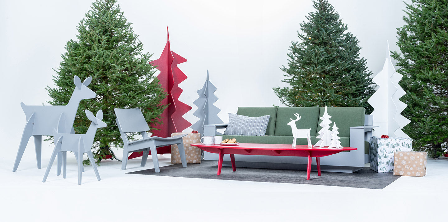 holiday decor of large and small reindeer and trees setup in a studio scene surrounded by pine christmas tress with a sofa cocktail table and lounge chair sitting on an area rug