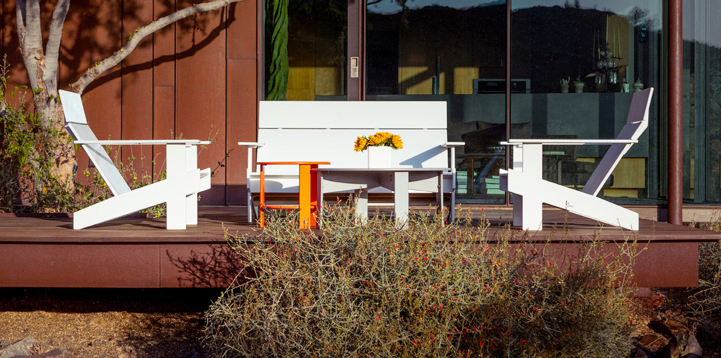 a white lollygagger sofa, 2 white lollygagger lounge chairs, orange lollygagger side table, and white round lollygagger cocktail table on wood deck.