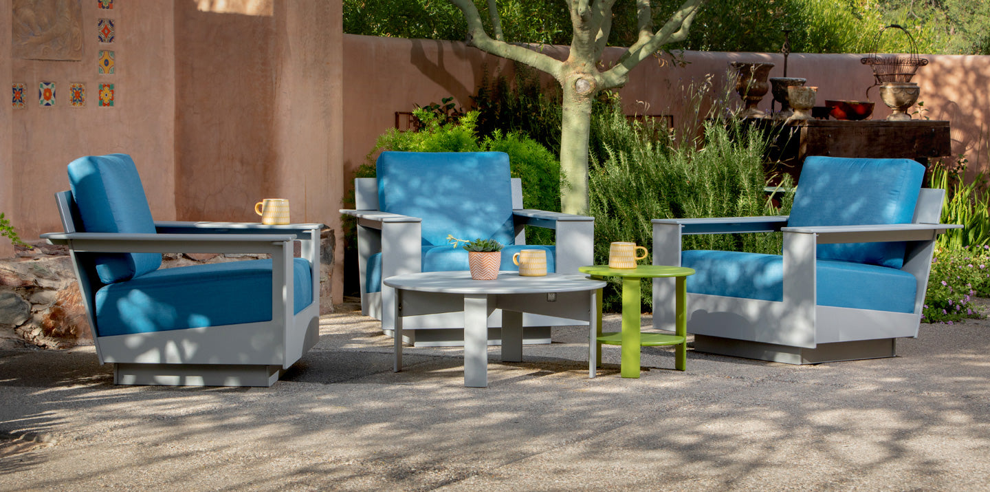 outdoor sofa with lounge chairs in grey frame and blue cushions with surfboard shaped cocktail table on a stone paver patio