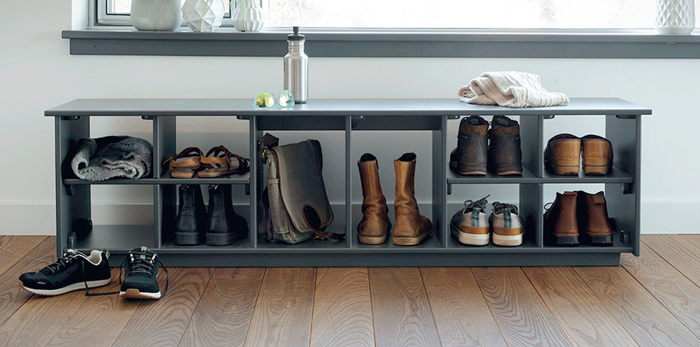 a charcoal cubby bench with boot holes inside a homes hallway with various boots and shoes stored. 