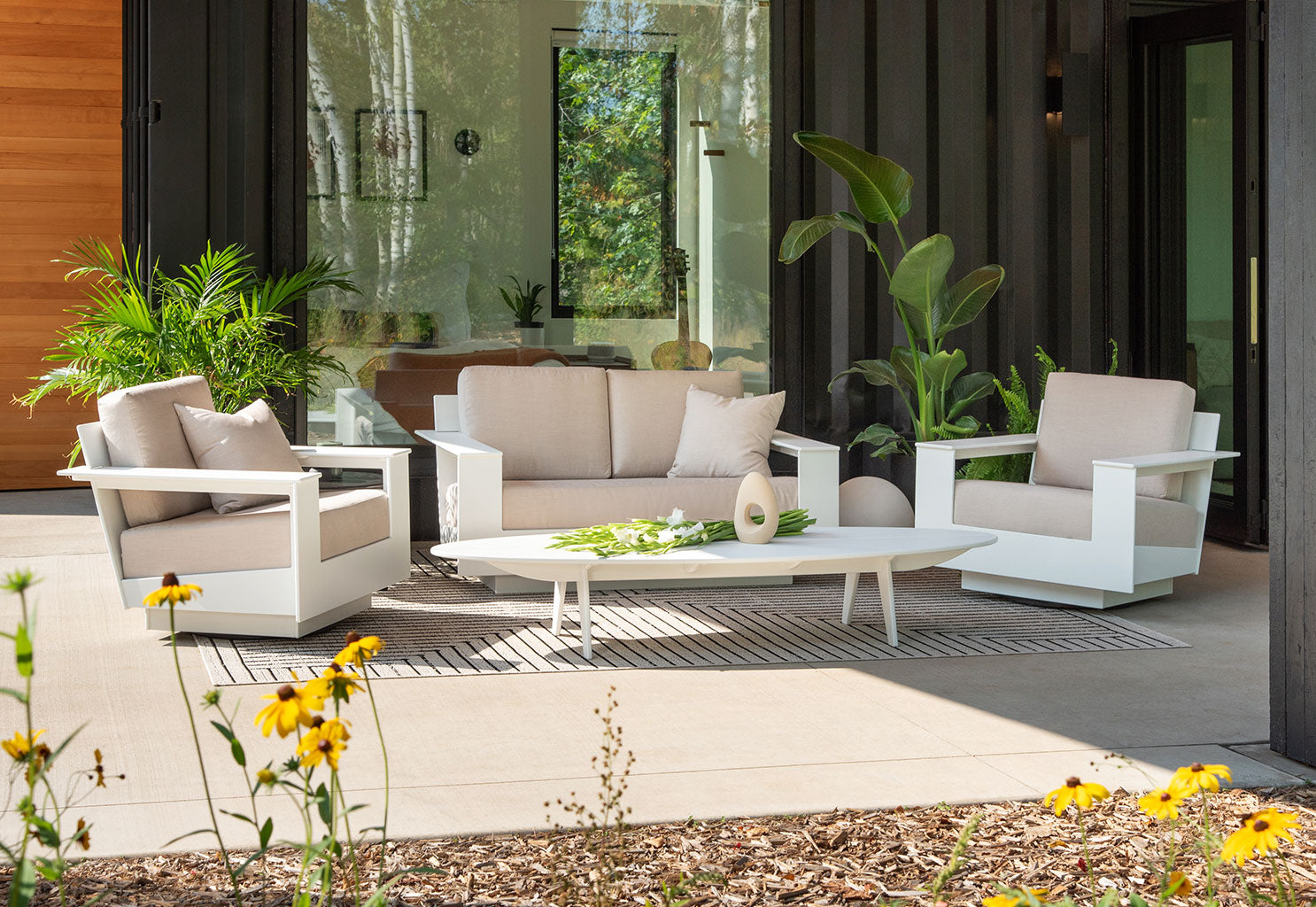 a nisswa love seat with two lounges arranged on a patio with a bolinas table.