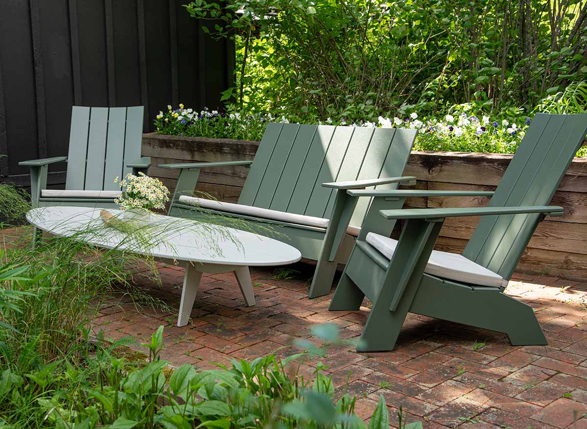 a sage adirondack bench with two sage adirondack chairs around a fog bolinas table on a stone patio