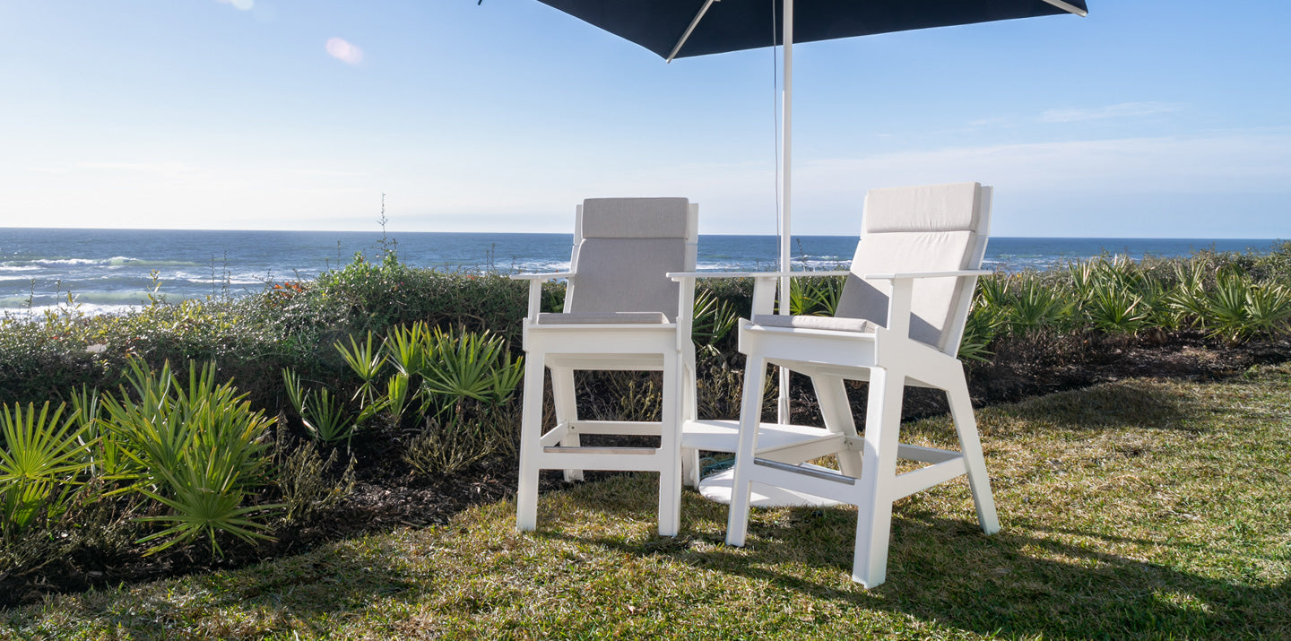 Two white tall lounge chairs beside a sunny ocean.