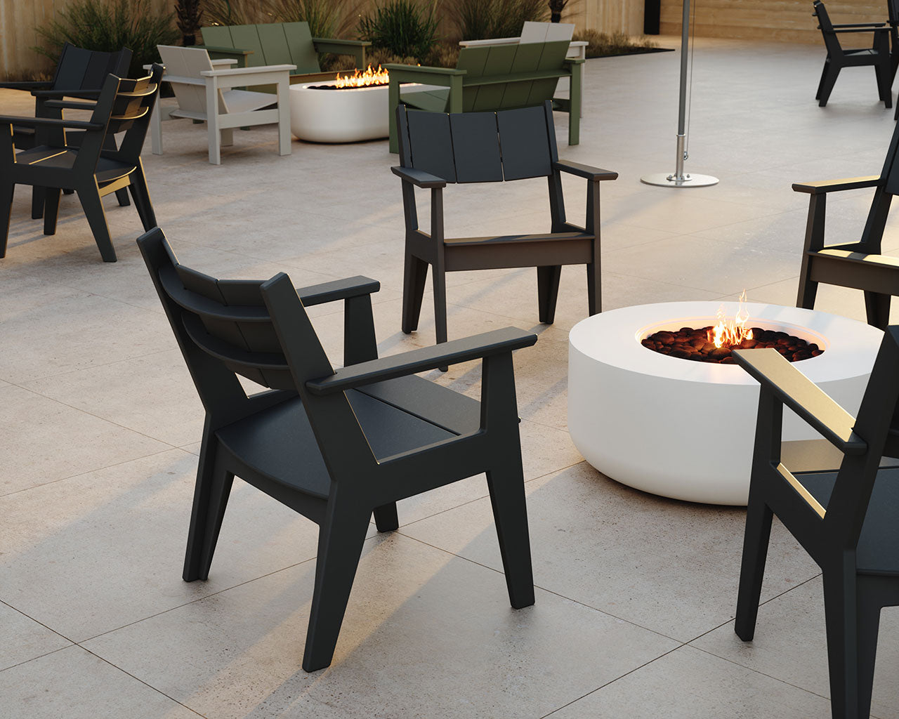 Modern outdoor patio furniture set featuring black Club-style armchairs arranged around a round white fire pit on a light stone tile patio.