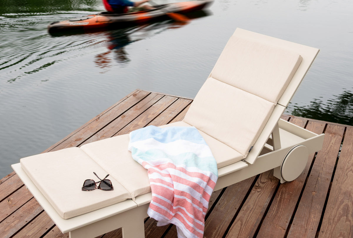 tall lollygagger chaise on a dock. a man in a kayak paddles in the water in the background.