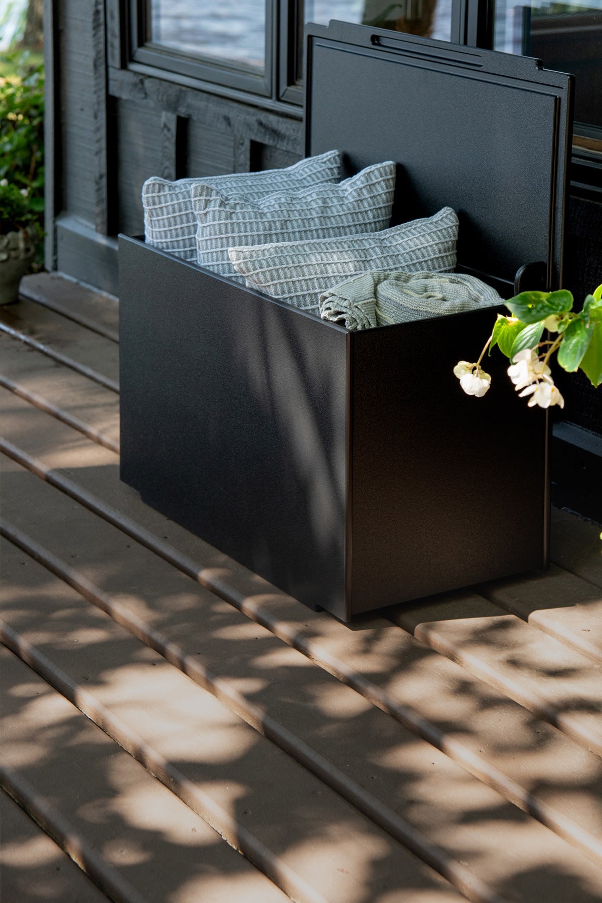 A black mondo double storage with it's lid open showing that it's storing pillows on a wood deck