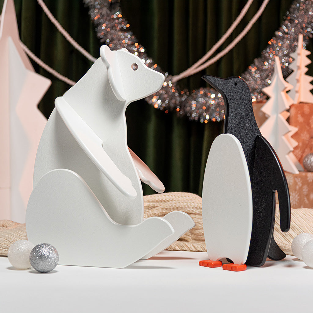 White bear and black penguin figurines on a decorative background with Christmas lights.