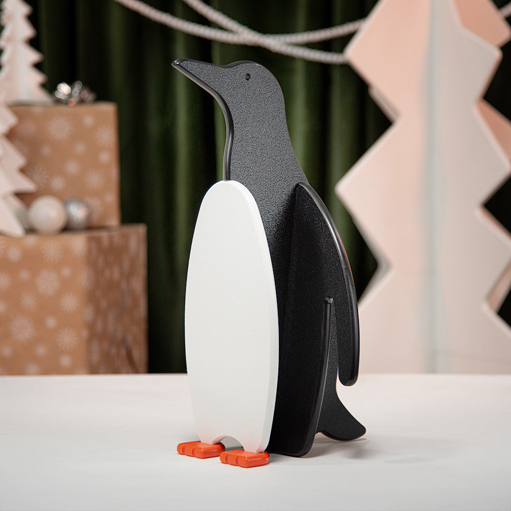 Penguin-shaped decorative item on a white surface with a festive background