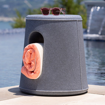 blue speckle dewey stool on the edge of a pool. a pink towel is rolled and in the center of stoo with a pair of sunglasses on top. 