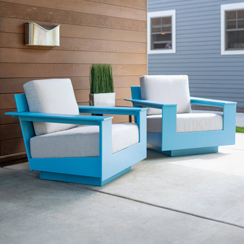 two sky blue nisswa lounge chairs with silver cushions sitting side by side on a stone patio along wooden wall. 