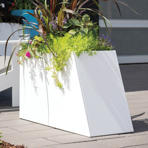 white tessellat slope planter with greenery on a stone patio.