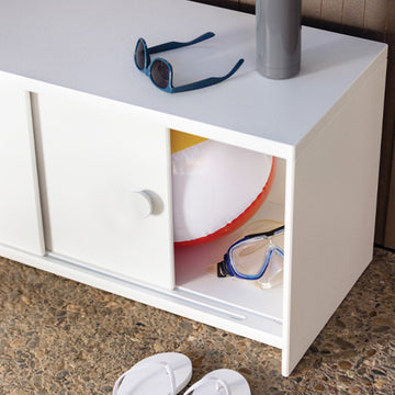 white slider credenza on stone patio with right door slid open. various beach accessories are in the credenza.