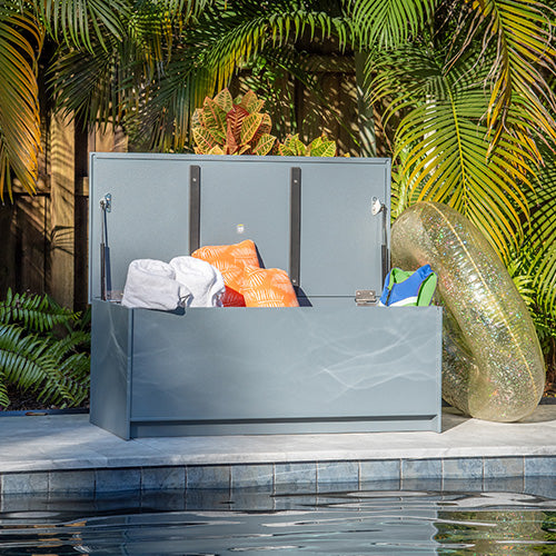 Gray outdoor storage box with items on a patio with plants in the background