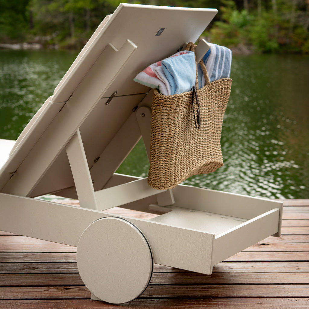 close up of the back of a tall chaise showing the bag hook in use. a wicker bag with towels is hanging from the hook. 